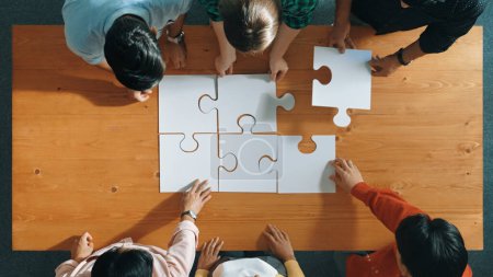 Photo for Top down view of skilled business people assemble jigsaw puzzle on meeting table. Group of diverse team working together to solve the puzzle. Represented unity, togetherness, cooperative. Convocation. - Royalty Free Image