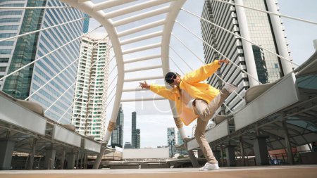 Téléchargez les photos : Homme asiatique élégant effectuer la danse hiphop avec caméra à faible angle. Brisez le danseur en montant l'escalier tout en écoutant de la musique du casque et en dansant ensemble en ville. Sport de plein air 2024. Brillamment. - en image libre de droit