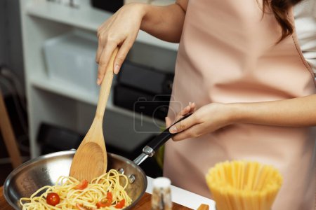Close up of hand chef influencer cooking spaghetti mix ingredient taking to frying pan, putting seasoning and tasty sauce to make good flavor, Concept of presenting homemade food at studio. Postulate.