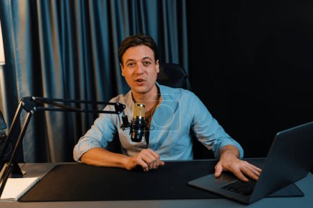 Photo for Host channel smart broadcaster talking on live social media application searching on laptop, broadcasting streamer wearing headphone using mic at modern home office studio in warm lighting. Pecuniary. - Royalty Free Image