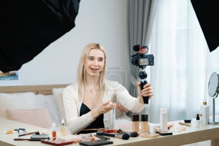 Mujer joven haciendo belleza y contenido de vídeo tutorial cosmético para las redes sociales. El blogger de belleza sonríe a la cámara mientras muestra cómo aplicar el cuidado de la piel de belleza a la audiencia o seguidores. Blithe.