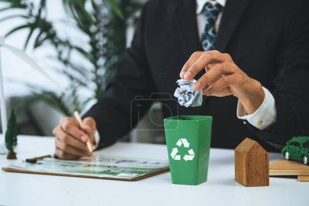 Foto de Empresario puso residuos de papel en una pequeña papelera de reciclaje en su oficina simbolizan el esfuerzo corporativo en la gestión de residuos ecológicos mediante el reciclaje de un medio ambiente más verde y la contaminación cero. Gyre. - Imagen libre de derechos