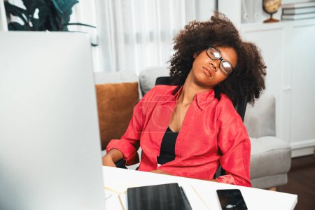 Foto de Joven mujer africana tomando una siesta con vestido encima del traje de color, apoyándose en la silla de la oficina en el lugar de trabajo, guardando gafas mientras duerme. Concepto de agotamiento del trabajo en proyectos de trabajo. Tastemaker. - Imagen libre de derechos