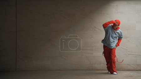 Téléchargez les photos : Belle chorégraphe pratique la danse de rue en arrière-plan gris. Jeune danseur b garçon attrayant effectuer tout en portant un tissu élégant. Sensation de pas animé. Espace de copie. Sport de plein air 2024. Brillamment. - en image libre de droit