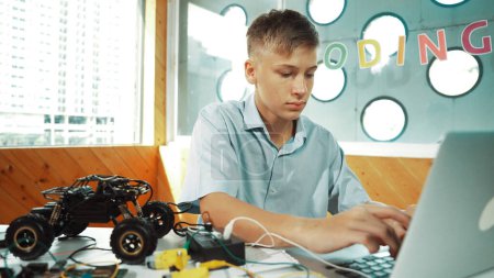 Schlaue Studenten arbeiten am Laptop, während sie den Modellbau von Autos analysieren. Glücklicher Highschool-Junge, der den Computer benutzt, um mit einem elektronischen Werkzeug die Struktur von Robotermodellen zu studieren oder zu lernen. Erbauung.
