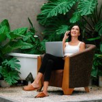 Modern young woman working remotely or relaxing in the solitude of a minimalist architectural concrete style summer exotic plant foliage garden, surrounded by tropical plants. Blithe