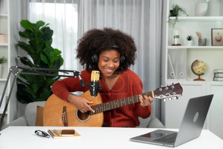 Photo for Host channel in musician of young African American playing guitar along with singing, broadcasting on laptop in studio. Decoration of equipment of headsets and recording microphone. Tastemaker. - Royalty Free Image