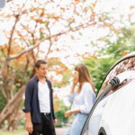 Lovely young couple recharging battery for electric car during autumnal road trip travel EV car in autumnal forest. Eco friendly travel on vacation during autumn. Exalt