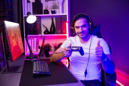 Photo for Smart gaming streamer with joystick player looking at camera, playing battle team shooting gun background at warship on pc screen at side view, wearing headset at digital neon light studio. Surmise. - Royalty Free Image