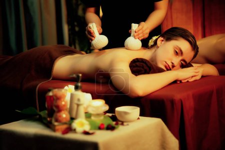 Photo for Hot herbal ball spa massage body treatment, masseur gently compresses herb bag on couple customer body. Serenity of aromatherapy recreation in warm lighting of candles at spa salon. Quiescent - Royalty Free Image
