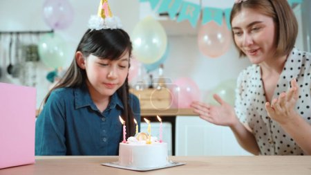 Energetic daughter and mother singing birthday song while clapping hand to music together. Caucasian mom celebrated birthday while using cake at dinning room decorated with colorful balloon. Pedagogy.