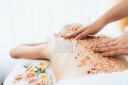 Photo for Closeup woman customer having exfoliation treatment in luxury spa salon with warmth candle light ambient. Salt scrub beauty treatment in health spa body scrub. Quiescent - Royalty Free Image