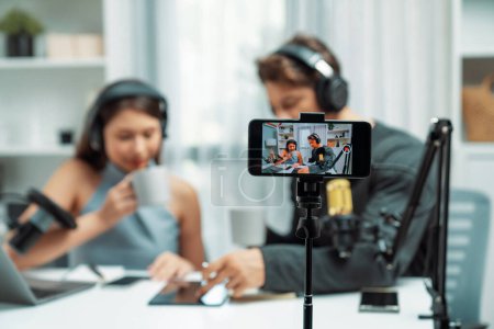 Focus on smartphone recording with blurry host channel broadcasters background making advice problem in live streaming with listeners with set live on talking show radio at modern studio. Postulate.