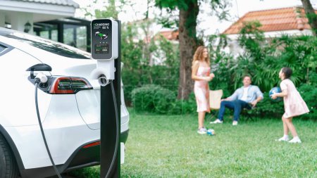 Photo for Focus electric vehicle recharge from home charging station on blur background of happy and playful family playing together. EV car using alternative and sustainable energy for better future.Synchronos - Royalty Free Image