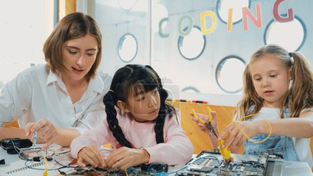 Qualifizierte kaukasische Lehrer unterrichten und erklären Schüler über digitales elektrisches Werkzeug. Expertin Mädchen lernen elektronische Geräte und verwenden, um Motherboard am Tisch mit Chips und Drähten platziert zu fixieren. Erution.