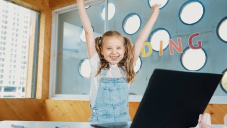 Photo for Happy girl looking at camera while raised hands to celebrate success project. Smart cute student finish writing, programing system and shouting with happiness in STEM technology class work. Erudition. - Royalty Free Image