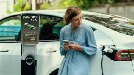 Photo for Electric vehicle recharging battery from home EV charging station using alternative energy with net zero emission on blurred background of young girl charging her car before vacation travel. Perpetual - Royalty Free Image