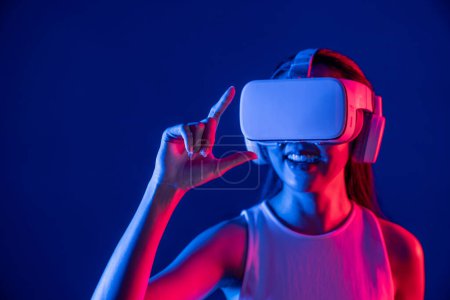 Foto de Mujer de pie rodeada de neón luz desgaste VR auriculares que conectan metaverso, futurista tecnología de la comunidad del ciberespacio, extendiendo índice y dedo pulgar interactuando objeto virtual. Alucinaciones. - Imagen libre de derechos