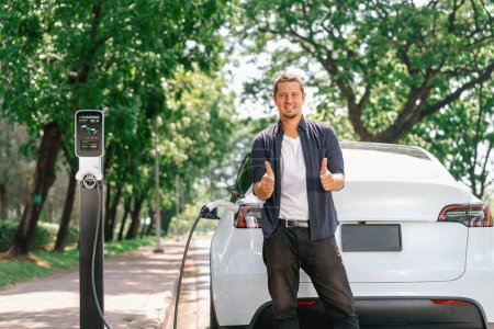 Mann lädt Batterie für Elektroauto während der Fahrt Elektroauto in Naturwald oder Nationalpark. Umweltfreundliches Reisen im Urlaub und im Urlaub. Erhöhen