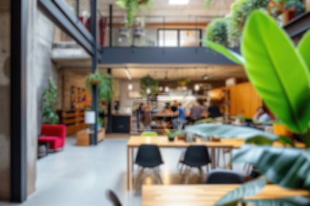 Defocused image of a lively modern co-working area with people and indoor plants. Resplendent.