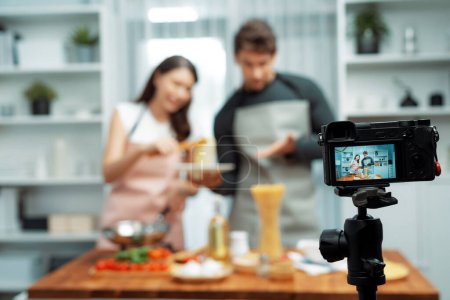 Photo for Couple chef influencers cooking special homemade of spaghetti with tongs taking to frying pan, putting seasoning and tasty sauce to make good flavor, recording on camera with live chanel. Postulate. - Royalty Free Image