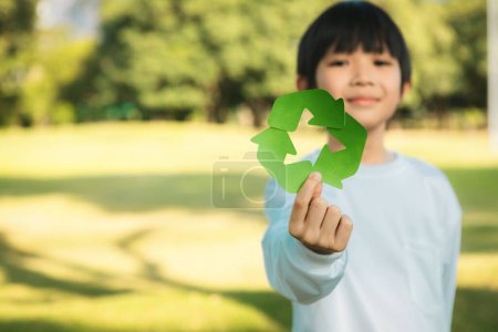 Foto de Joven niño asiático alegre sosteniendo símbolo de reciclaje en el parque verde natural de luz natural que promueve el reciclaje de residuos, reducir y reutilizar el estímulo para la conciencia ecológica sostenible para la generación futura. Gyre. - Imagen libre de derechos