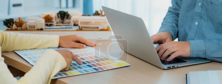 Der Innenarchitekt wählt die Farbe aus, indem er Farbmuster verwendet, während sein Kollege Informationen mit dem Laptop sucht. Kreatives Design und Teamwork-Konzept. Nahaufnahme. Bunt gemischt.