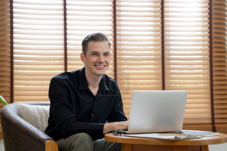 Foto de Retrato de un psicólogo masculino feliz y sonriente sentado en un sillón usando una computadora portátil para diagnóstico mental en la sala de la oficina de psiquiatría. Terapeuta mental amigable y profesional. Revelación - Imagen libre de derechos