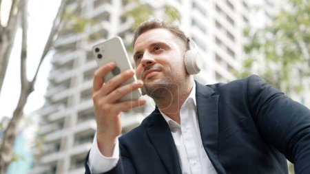 Photo for Business people wear headphone to listen relaxing music while look at phone to check sales report from marketing team in green city. Happy project manager move to song while hold telephone. Urbane. - Royalty Free Image