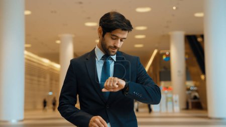 Photo for Caucasian smart business man looking at watch while waiting colleague. Executive manager wearing suit while standing at mall with blurred background. Investor wear blue suit check time. Exultant. - Royalty Free Image