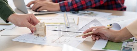 Photo for Skilled architect team using architectural equipment during colleague discussion about building design at meeting table with blueprint scatter around. Closeup. Focus on hand. Delineation. - Royalty Free Image