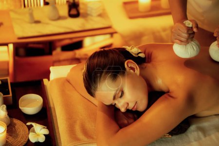 Photo for Hot herbal ball spa massage body treatment, masseur gently compresses herb bag on woman body. Tranquil and serenity of aromatherapy recreation in warm lighting of candles at spa salon. Quiescent - Royalty Free Image