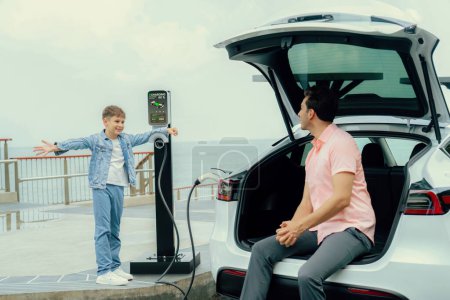 Photo for Family road trip vacation traveling by the sea with electric car, father and son recharge EV car with green and clean energy. Natural travel and eco-friendly car for sustainable environment. Perpetual - Royalty Free Image