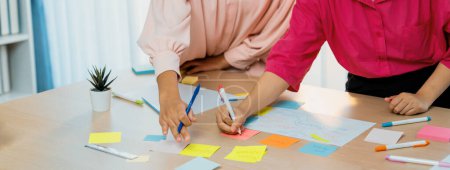 Photo for Group of young business group brainstorms ideas on colorful sticky notes. A portrait of startup group planing marketing strategy while writing down on sticky note at office meeting room. Variegated. - Royalty Free Image