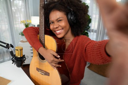 Photo for Host channel in musician of young African American with selfie for fans, broadcasting on smartphone in private studio. Decoration of equipment of headsets and recording microphone. Tastemaker. - Royalty Free Image