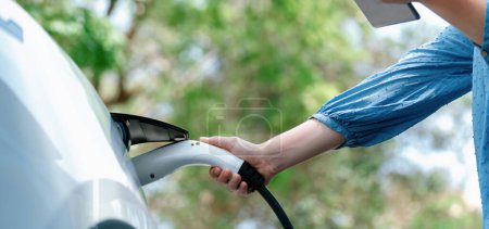 Photo for Panorama road trip vacation by the green countryside nature with beautiful young woman checking battery status from smartphone while recharging electric car. Eco-friendly travel wit EV car. Perpetual - Royalty Free Image