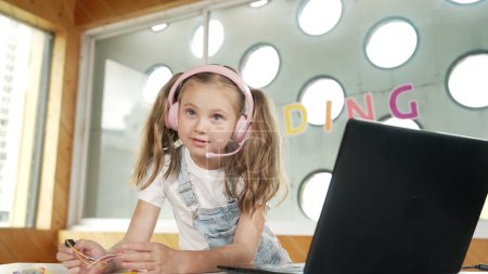 Photo for Girl wearing headphone while study equipment and looking at camera. Caucasian child doing science experiment with laptop, screwdriver and wires placed near on table. Smart online classroom. Erudition. - Royalty Free Image