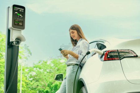 Junge Frau nutzt Smartphone-Online-Banking-App, um im Urlaub im Nationalpark oder im Sommerwald an der Ladestation für Elektroautos zu bezahlen. Erhöhen