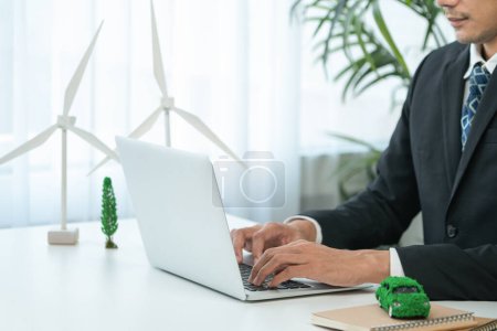 Businessman working in office developing plan or business project on eco-friendly ev car using net zero alternative energy technology on computer for greener environment as apart of CSR effort. Gyre