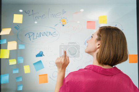 Photo for Young beautiful businesswoman putting sticker on glass board while finding a solution to solve financial problems by using mind map and colorful sticky note. Creative business concept. Immaculate. - Royalty Free Image