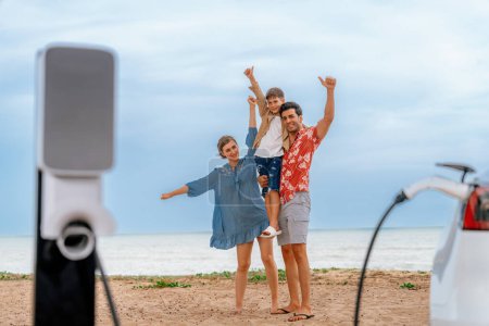 Photo for Family vacation trip traveling by the beach with eco-friendly electric car, lovely and cheerful family charging EV car battery on the seascape with green and sustainable energy. Perpetual - Royalty Free Image