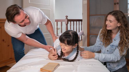 Glückliche moderne Familien wecken ihr kleines Mädchen am Wochenende mit spielerischem Kitzeln, indem sie ihre Liebe und Zuneigung zu ihrer kleinen Tochter zum Ausdruck bringen, gemeinsam lachen und lächeln. Panorama-Synchronen