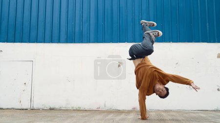 Téléchargez les photos : L'homme hispanique tend les bras et danse la rue en dansant devant le mur. Motion shot du danseur ou chorégraphe élégant en tenue décontractée pratiquant la danse dans le style hip hop. Sport de plein air 2024. Endeavor. - en image libre de droit