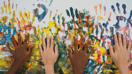 Téléchargez les photos : Heureuse main étudiante diversifiée placée sur un mur coloré. Gros plan d'une main multiculturelle ou d'enfants de races mixtes peignent leur empreinte à la salle d'art. Contexte. Activité créative. Édification. - en image libre de droit