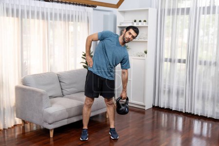 Photo for Athletic body and active sporty man lifting kettlebell weight for effective targeting muscle gain at gaiety home as concept of healthy fit body home workout lifestyle. - Royalty Free Image