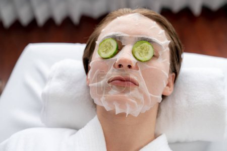 Téléchargez les photos : Ambiance de jour sereine du salon de spa, la cliente se délecte de rajeunir avec un masque facial luxueux au concombre. Soins du visage et soins de beauté concept. Tranquillité - en image libre de droit