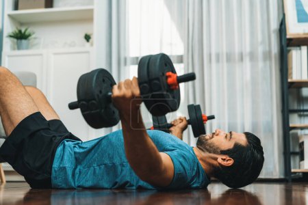 Photo for Athletic body and active sporty man lifting dumbbell weight for effective targeting muscle gain at gaiety home as concept of healthy fit body home workout lifestyle. - Royalty Free Image