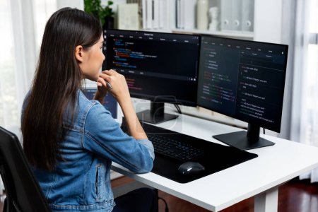 Photo for Young Asian IT developer looking online information on pc for beautiful pose with coding program data of website application, wearing jeans shirt. surround by safety analysis two screens. Stratagem. - Royalty Free Image