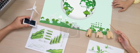Photo for Green city poster was placed on green business meeting room. Professional architect hand holding wind mill model represented renewable energy. Green design. Closeup. Top view. Delineation. - Royalty Free Image