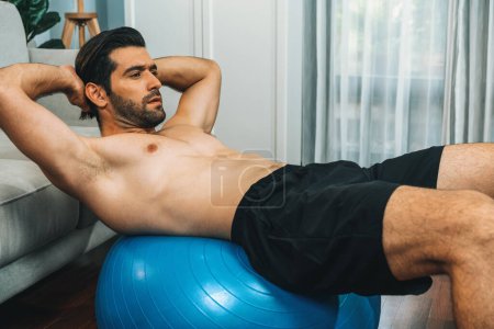 Photo for Athletic and sporty man doing situp on fitness ball during home body workout exercise session for fit physique and healthy sport lifestyle at home. Gaiety home exercise workout training concept. - Royalty Free Image